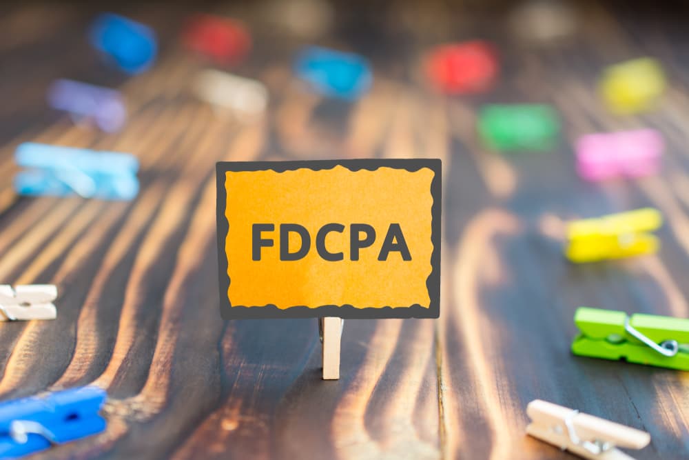 Signboard displaying 'FDCPA, Fair Debt Collection Practices Act' on a wooden background with colorful clothespins surrounding it.