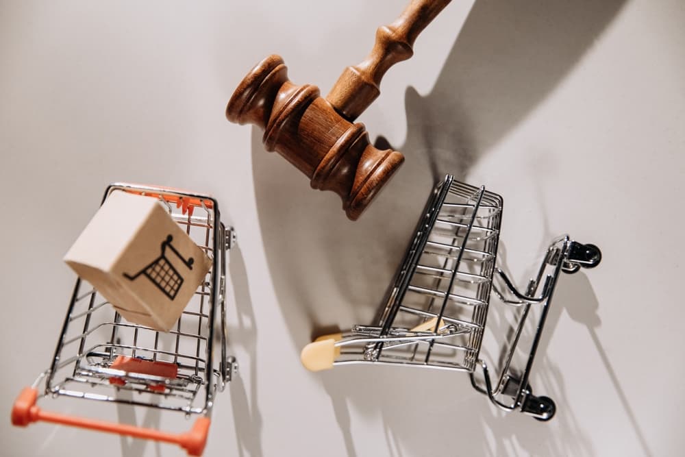 A judge's gavel next to two small shopping carts and a box with a cart icon.