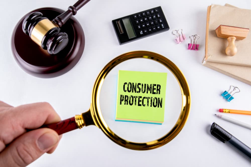 A magnifying glass focusing on a note labeled "Consumer Protection" beside a gavel and calculator.