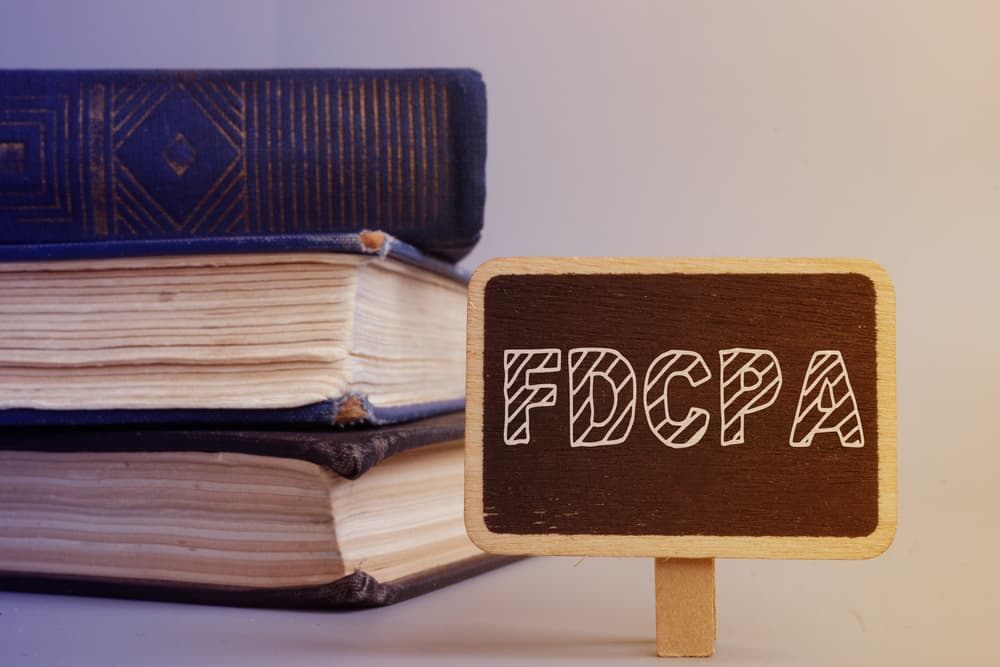 A small chalkboard with "FDCPA" written on it, placed in front of old books.