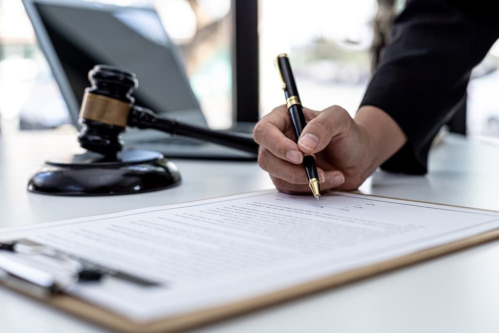 A male lawyer signs a plea agreement with a client in a fraud case involving litigation against a company employee. Illustrates legal proceedings in fraud cases