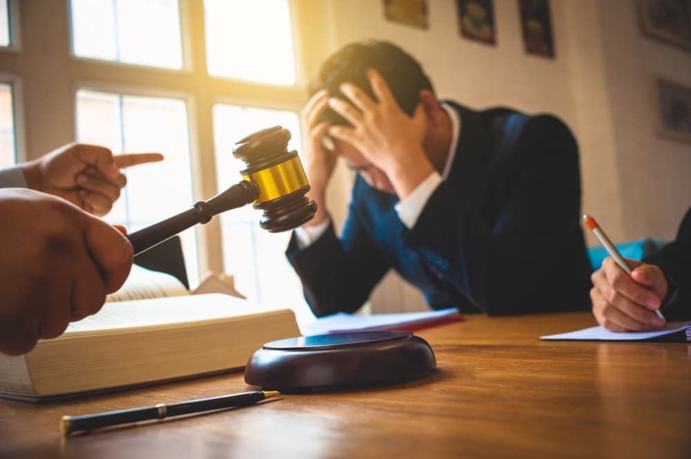 Stressed man in court with a judge's gavel, lawyer, and accuser pointing.