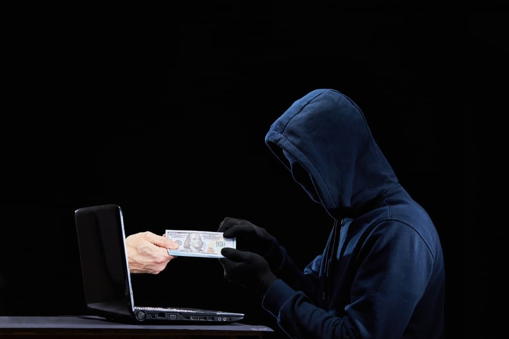 Hacker illegally receiving money online, holding cash from a laptop. Concept for computer hacker, network security, cyber attack, and virus.