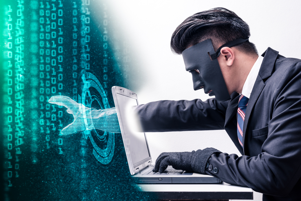 A hacker's hand extending through a laptop screen to steal data.