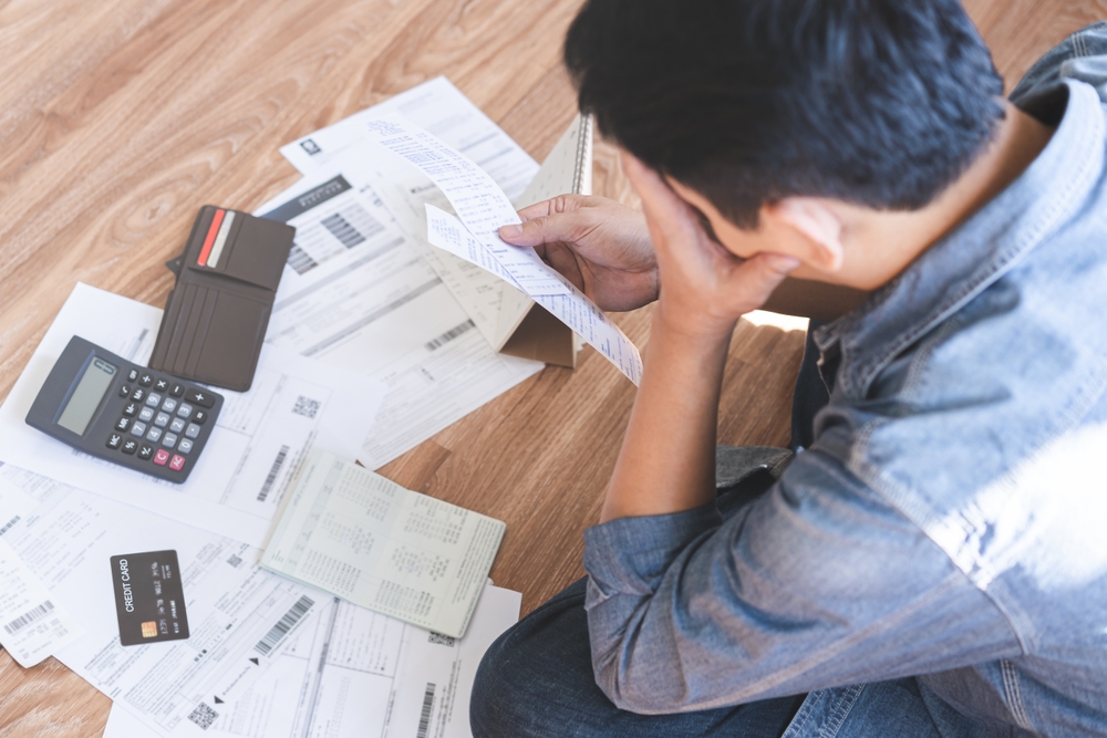 Financial concept: an Asian young man stressed and confused by errors in his credit report, affecting his ability to pay bills.