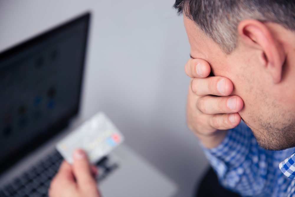 Frustrated man holding a credit card while looking at a laptop screen