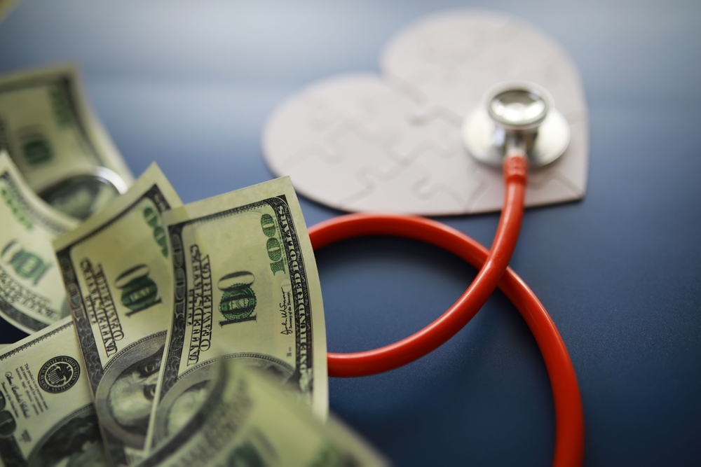 Stethoscope placed on a pile of money beside a heart-shaped puzzle piece, representing the financial impact of healthcare and medical debt