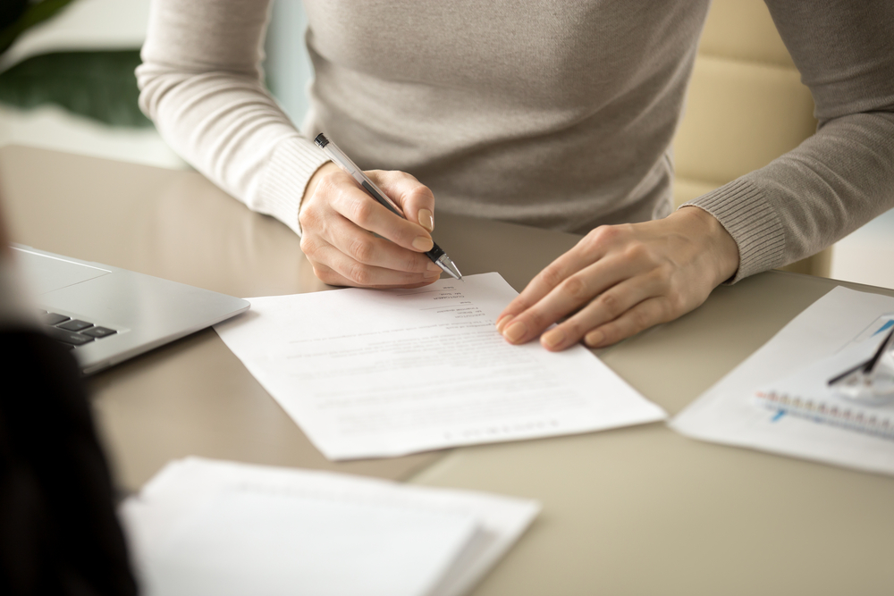 Woman signing a written contract of debt collection, focusing on her hand holding a pen and putting her signature on the official document.