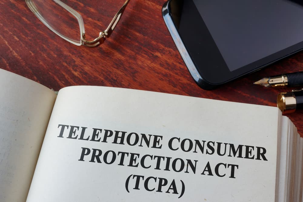 The image shows a book titled "Telephone Consumer Protection Act (TCPA)" next to a phone.